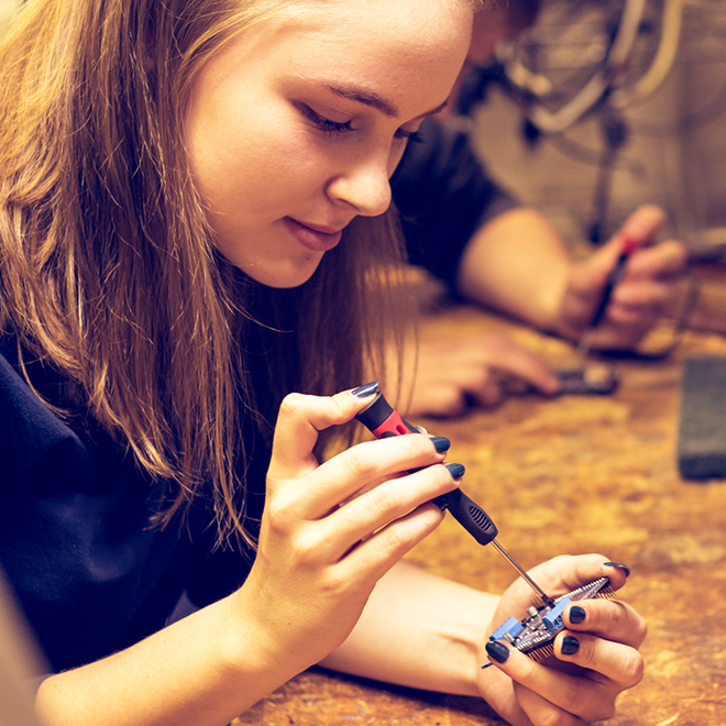 young woman using a screwdriver on a circuit board